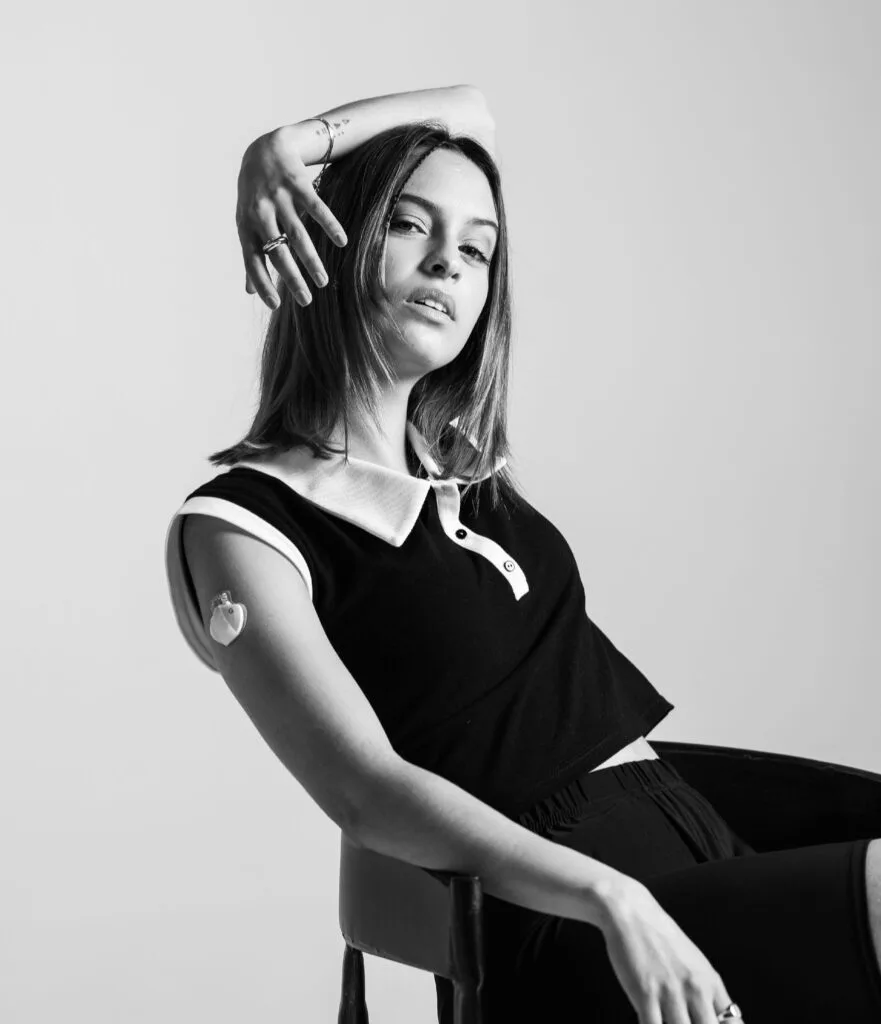 mujer posando para la camara con una bomba de insulina en su brazo derecho.